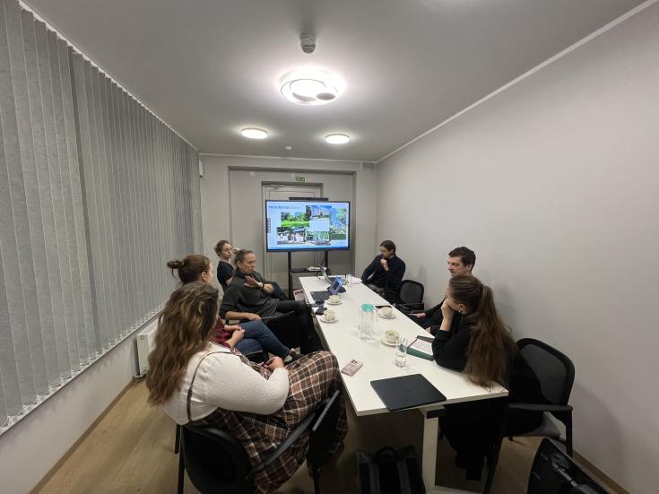PROXIMITIES stakeholder group- Riga Planning Region PROXIMITIES stakeholders from the Riga Planning Region discuss a presentation on "PROXIMITIES Olaine" in a meeting room. The screen displays project visuals, and the table holds coffee cups, water glasses, and notebooks.