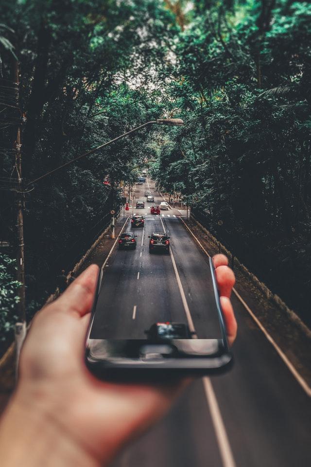 Person holding phone out of which a road appears