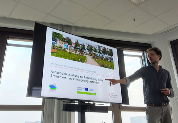 Dark-haired man presents power point slides in the front of big screen.