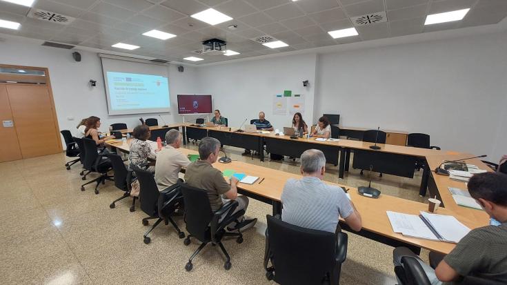 People sitting in a meeting room (horse-shoe tables display) and with a screen on the empty side