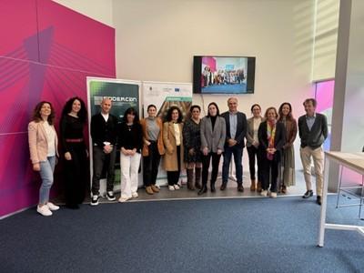 13 people stand in front of a standee, a pink wall and a TV screen