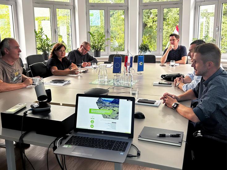 Stakeholders attending the third GIFT Project Regional Stakeholder Group meeting in Zagreb, August 2024. Participants are seated around a conference table, engaged in discussions with a laptop displaying the GIFT project presentation in the foreground. European Union and Croatian flags are on display.