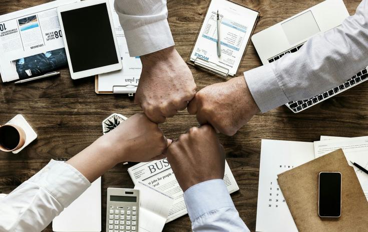 Four fists meeting in a gesture of cooperation over a table