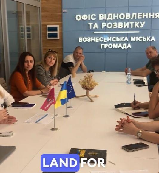 People sitting at around a table, and there is writing in Ukranian on the back wall.