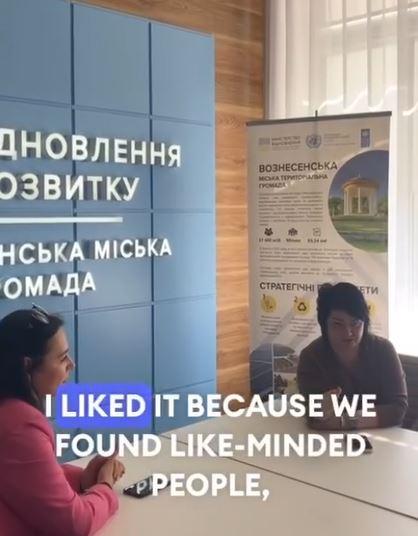 Two women sit at a table. Behindi them is writing in the Ukrainian language. English subtitles relay the speaker's message