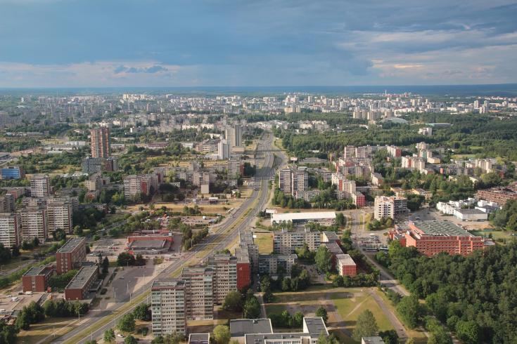 Aerial view of Vilnius, the capital city of Lithuania, showcasing its urban landscape, modern architecture, and green spaces, with vast stretches of forests visible in the background.