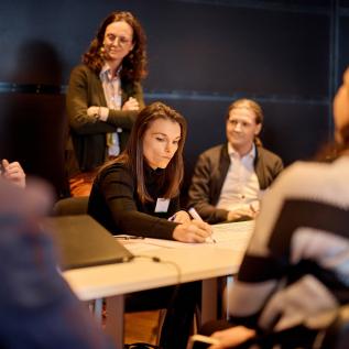 Person writing on paper with people standing around