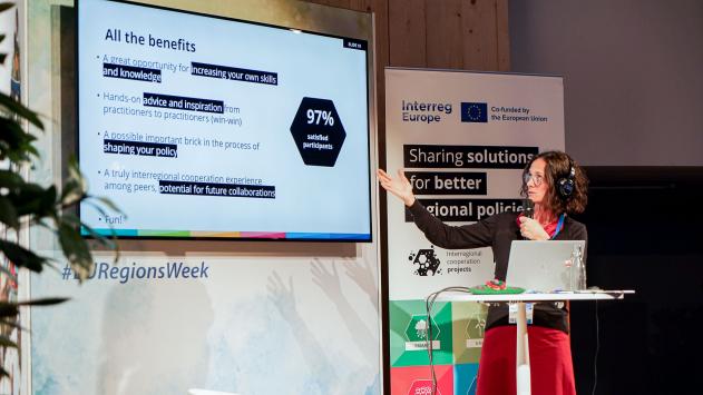 Peer review talk at the European Week of Regions and Cities 2023 a person presenting next to a screen with the presentation slides