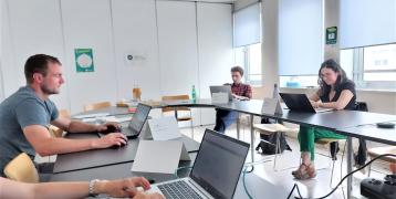 Four people gathered in a bright meeting room around two tables.