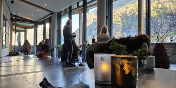 Photo of a cowork facilities with people sitting by a stretch of window. Outside there are mountains.