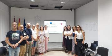 Group photo in a room. Adults watch the camera, behind them a powerpoint slide on a screen