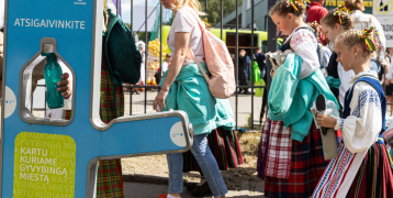 People in regional costumes passing by a mobile water fountain.