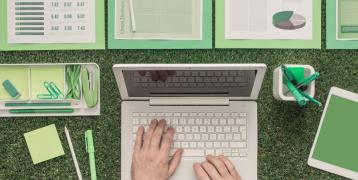 A person with a laptop where all the items on the table relate to green for business 