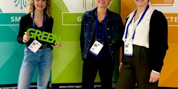 3 women standing, one with a sign with the word green on her hands