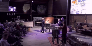 Panelists and a moderator on stage with a public in the barn