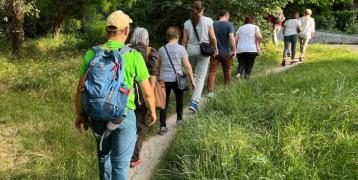 City of Trails Reggio Emilia People walking in line on a trail, immersed in greenery, with hats and backpacks.