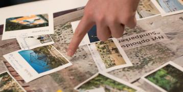 A finger points at some photographs spread out on a table.