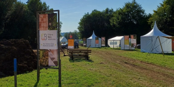 A sunny outdoor scene at the Demoforest 2024 forestry fair in Belgium, showcasing a wooden table in the foreground and a Filière Bois Wallonie promotional banner in the background, along with tents and other exhibition areas.