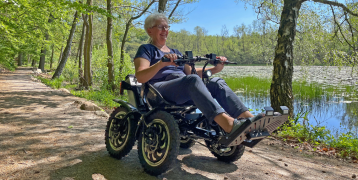A woman with white short hair on a wheelchair visits a green area on a sunny day