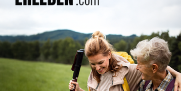 An adult woman and an elderly woman in an outdoor space holding walking poles.  