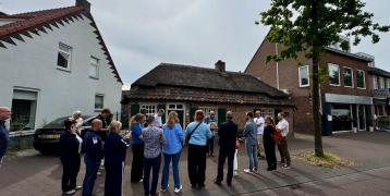 Group of people facing away from the camera are standing in the street in front of houses. 