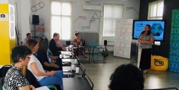 Stakeholders sit in a room and watch a women present the SKYLA project