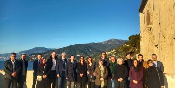 Around 20 people are gathered in front of the sea and moutains