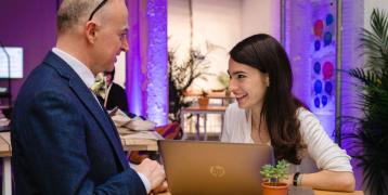 Interreg Staff speaks to project partner from a high table in front of a laptop at an event.