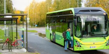 Green electric bus stopped on a bus stop and girl getting on the bus.