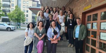 The group of INVOLVIM project participants poses in front of a typical Finnish red brick building housing the immigration office "Moni," where they had a study visit.