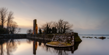 Historic stone ruins on the edge of Lough Derg, reflected in still waters at dusk.