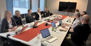 A group of people is sitting around a meeting table in a meeting room.