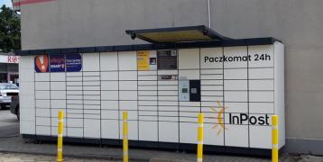 The picture depicts an Automated Parcel Machine situated next to a local supermarket, close to a residential neighborhood.