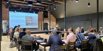 A large room set out with tables and chairs in a 'U' formation with project partners presenting their SWOT and PESTEL analyses to the audience in Kalevan Navetta.