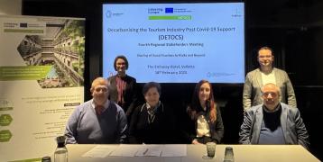 Six people sit at a table in front of a presentation facing the camera 