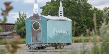 A tiny house on wheels which resembles a tiny townhall.