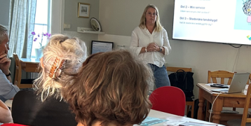 Person standing at top of room presenting to a group of people 