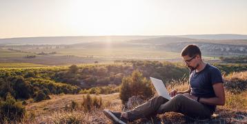 man using a laptop on a cliff