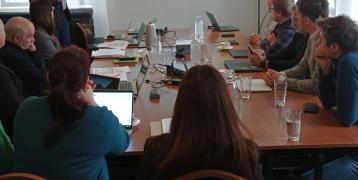 I see many people around a table looking at a screen