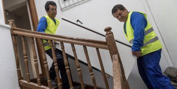 Two men lowering a fride by the stairs.