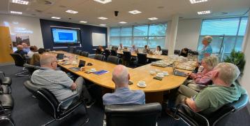A group of people in a meeting room hearing a presentation