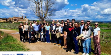 A group of PROXIMITIES project partners from across Europe pose together outdoors during a study visit to Manresa, Spain. They stand on a rural path with green fields, a large tree, and a historic building in the background under a partly cloudy blue sky. Interreg Europe and PROXIMITIES logos appear in the bottom-left corner.
