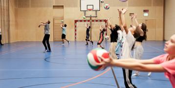 Children practicing volleyball skills in an indoor sports hall