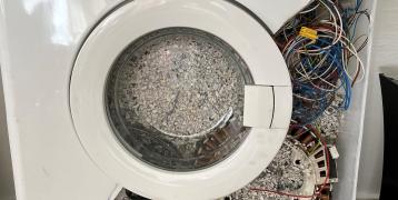 A close up of a washing machine filled with cables and other discarded parts of electronic devices