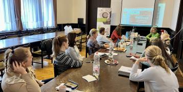 Participants during the 4th stakeholder meeting of the Hajdú-Bihar County sitting around a table, listening to a presentation on the project activities from the previous period