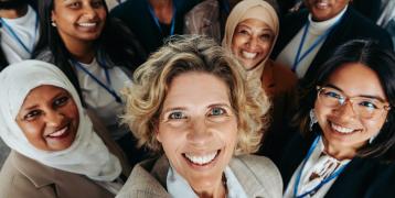 The image depicts a mature woman leading a diverse team with enthusiasm and professionalism