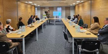People attending a Local Stakeholder Group (LSG) meeting for the ADAPTO project in Lubelskie Voivodeship. A speaker is presenting in front of a screen showing a map, while participants sit around a U-shaped table.