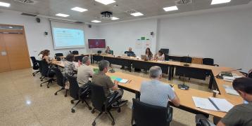 People sitting in a meeting room (horse-shoe tables display) and with a screen on the empty side