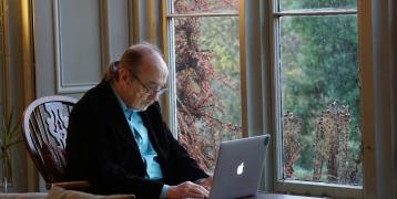 Older gentleman sitting in a chair by the window using a laptop