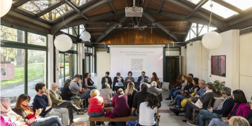 Neighbourhood Houses Group of people meeting in a building with wooden beams and large windows, looking at a screen with a QR code to collect inputs